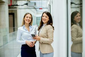 två ung företag kvinnor med mobil telefon i de kontor hall foto