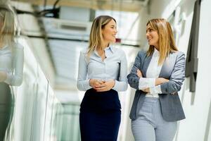två ung företag kvinnor gående och diskuterar i de kontor hall foto
