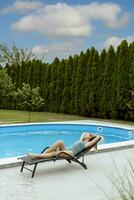 ung kvinna liggande på en däcksröding vid poolen i husets bakgård foto