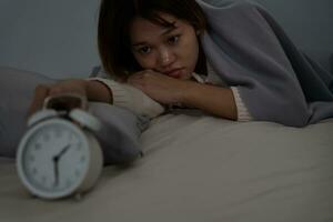 asiatisk kvinna i säng sent påfrestande till sömn lidande sömnlöshet, sömnlös eller rädd i en mardröm, ser ledsen orolig och stressad. trött och huvudvärk eller migrän vakna upp i de mitten av de natt. foto