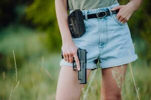 en flicka i denim shorts och med en pistol i henne hand poser för en Foto.. närbild foto