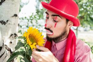 en rörande och överraskad mima beundrar de blomma. clown finputsning de kronblad av en solros. foto