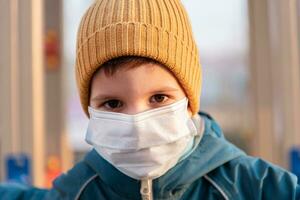 porträtt av en ung barn i en medicinsk mask på de gata under de coronavirus och covid pandemi - 19 foto