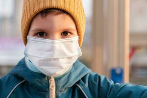 porträtt av en ung barn i en medicinsk mask på de gata under de coronavirus och covid pandemi - 19 foto