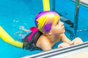 en små barn med en liv jacka på hans bröst är inlärning till simma i ett inomhus- slå samman. foto