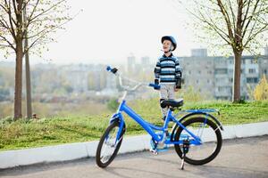 söt barn i hjälm och skydd står nära hans cykel foto