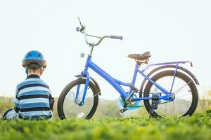 söt barn i hjälm och skydd sitter nära hans cykel foto