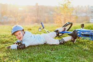 en små barn i en hjälm och skydd föll från en cykel till de gräs och var inte skadade foto