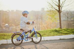 liten pojke i hjälm rider en cykel på en solig dag foto