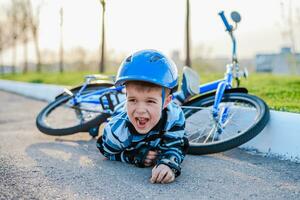 en små barn föll från en cykel till de väg, gråt och skrikande i smärta. foto