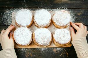 matlagning traditionell hanukkah sufganiyot. kvinna strössel munkar med pulveriserad socker. foto