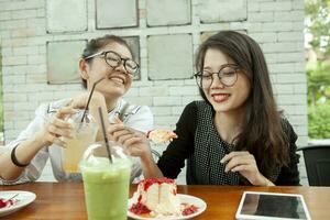 två asiatisk kvinna lycka känsla äter jordgubb ost kaka i Kafé foto