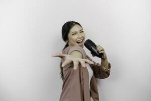 sorglös asiatisk kvinna är har roligt karaoke, sång i mikrofon medan stående över vit bakgrund foto