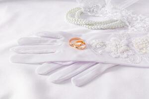 en par av guld bröllop ringar lögn på lyxig bröllop vit handskar. vit satin bakgrund med pärla pärlor. bröllop Tillbehör begrepp. foto