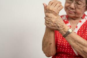 äldre asiatisk kvinna patienter lida från bedövande smärta i händer från reumatoid artrit. senior kvinna massage henne hand med handled smärta. begrepp av gemensam smärta, reumatoid artrit, och hand problem. foto
