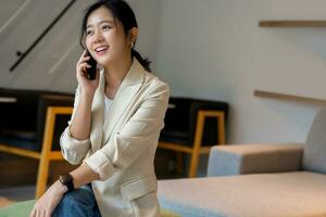 smart frilans asiatisk kvinna sitter och chatt med en kund på en cell telefon inuti en kaffe affär. med kopia Plats foto