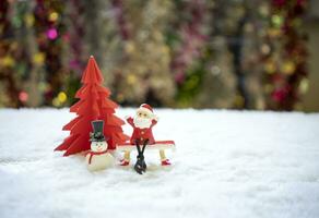 sata Sammanträde på röd bänk med snögubbe i främre av röd origami jul träd väntar för rolig festival, jul och ny år begrepp. foto