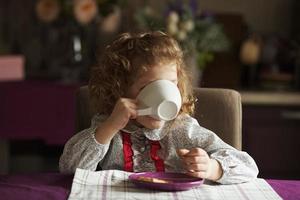 liten flicka som dricker från en stor vit kopp foto