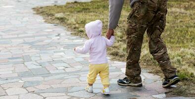 liten litet barn flicka går hand i hand med pappa utomhus. militär man i overall leder barn förbi hand. minne dag. fars dag. Lycklig familj. porträtt pappa och dotter. foto