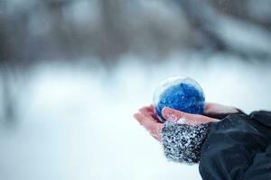 jul träd leksak i de händer av en barn. runda blå jul boll på snö bakgrund. foto