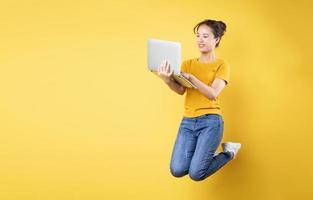 helkroppsprofilfoto av ung asiatisk tjej som hoppar högt och håller en bärbar dator som skriver ett nytt inlägg på sociala medier, isolerad på blå bakgrund foto
