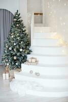 en stor jul träd i de levande rum, dekorerad med kransar och ljus ballonger. ljus jul interiör med en vit trappa. foto
