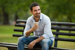 ung affärsman är dricka kaffe och vilar från arbete på de parkera foto