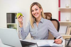 affärskvinna äter äpple medan arbetssätt i henne kontor foto