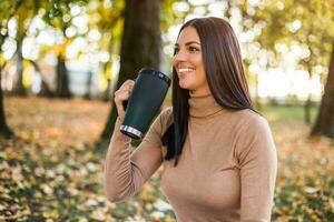 skön kvinna dricka kaffe medan åtnjuter i höst i de parkera foto