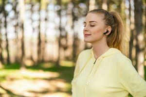 skön sportig kvinna med trådlös hörlurar åtnjuter lyssnande musik i de natur foto