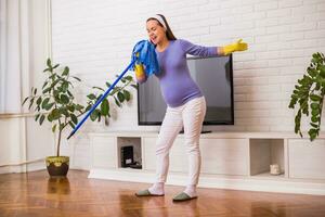 skön gravid kvinna åtnjuter rengöring henne hus. foto