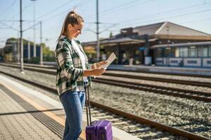 Lycklig kvinna ser på Karta medan stående på en tåg station foto