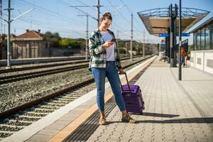 Lycklig kvinna använder sig av mobil telefon på en tåg station foto