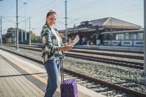 Lycklig kvinna ser på Karta medan stående på en tåg station foto