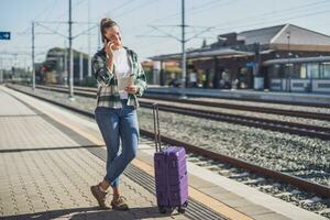 Lycklig kvinna använder sig av mobil telefon och innehav Karta på en tåg station foto