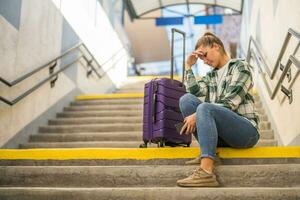 orolig kvinna med en telefon och resväska Sammanträde på en trappa på de tåg station foto