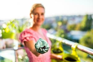 Lycklig kvinna är som visar jord för henne växter. fokus på jord. hon åtnjuter i trädgårdsarbete på balkong på henne Hem. foto