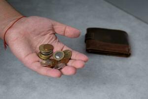 en man i hans handflatan innehar metall mynt och en läder plånbok lögner närliggande. selektiv fokus foto