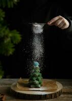 hand strössel glasyr socker på pepparkaka träd på mörk bakgrund. Semester och jul begrepp. hög kvalitet Foto