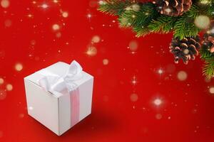 vit låda med gåva bunden med silke band med rosett och kvist av jul träd på de röd bakgrund foto