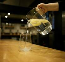 hand innehar en glas kanna av citronsaft och häller in i en glas glas. selektiv fokus.hög kvalitet Foto