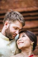 asiatisk brud och kaukasisk brudgum har romantisk tid med thailändsk klänning foto