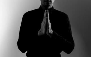 stilig man sitta bön på svart bakgrund. hans händer är bön- för guds välsignelser. foto