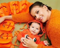 halloween porträtt av Lycklig ung mor och söt bebis bär orange pumkim jacka foto