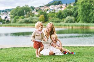 utomhus- porträtt av Lycklig ung mor med två härlig barn spelar förbi sjö eller flod på en trevlig sommar dag foto