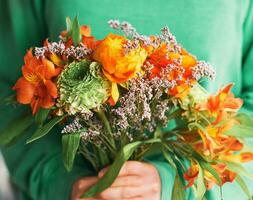 stänga upp porträtt av skön grön och orange ranunkel och alstroemeria bukett innehav förbi en person foto