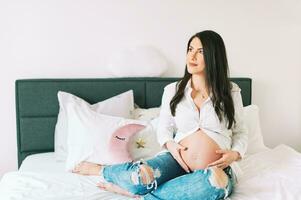 inomhus- porträtt av skön ung gravid kvinna vilar på säng foto