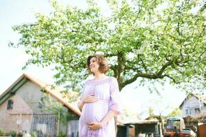 utomhus- porträtt av Lycklig gravid kvinna njuter trevlig solig dag i vår trädgård foto