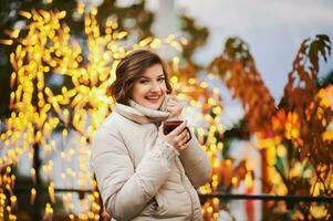 vinter- porträtt av Lycklig ung kvinna dricka varm choklad utanför på jul marknadsföra foto
