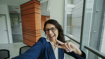 pOV av ung affärskvinna i kostym tar en selfie Foto innehav smartphone och ha roligt i modern kontor inomhus